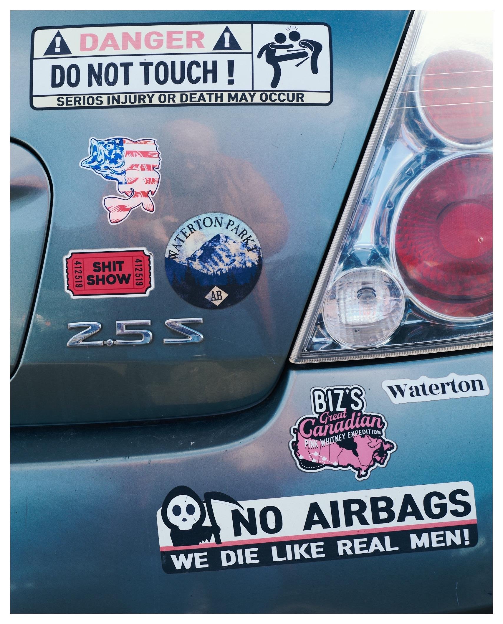 Right rear of a car with many stickers present.   "No airbags, we die like real men." and others of similar sentiment.