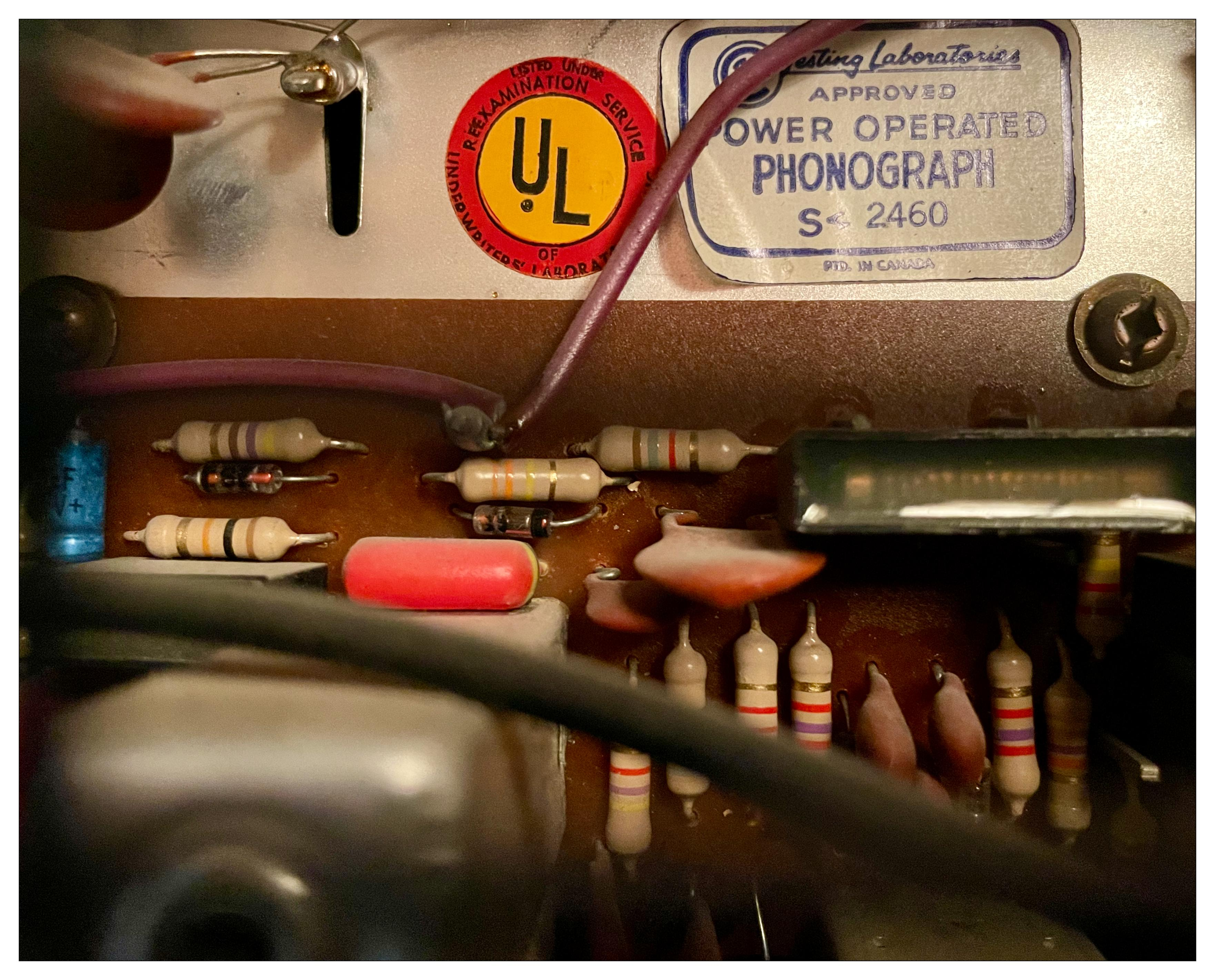 Close up of a discrete electronics board from a 1960s stereo.   There are many resistors, capacitors, etc all obviously had soldered in place.  There are some labels with very old underwriter lab logo and such.