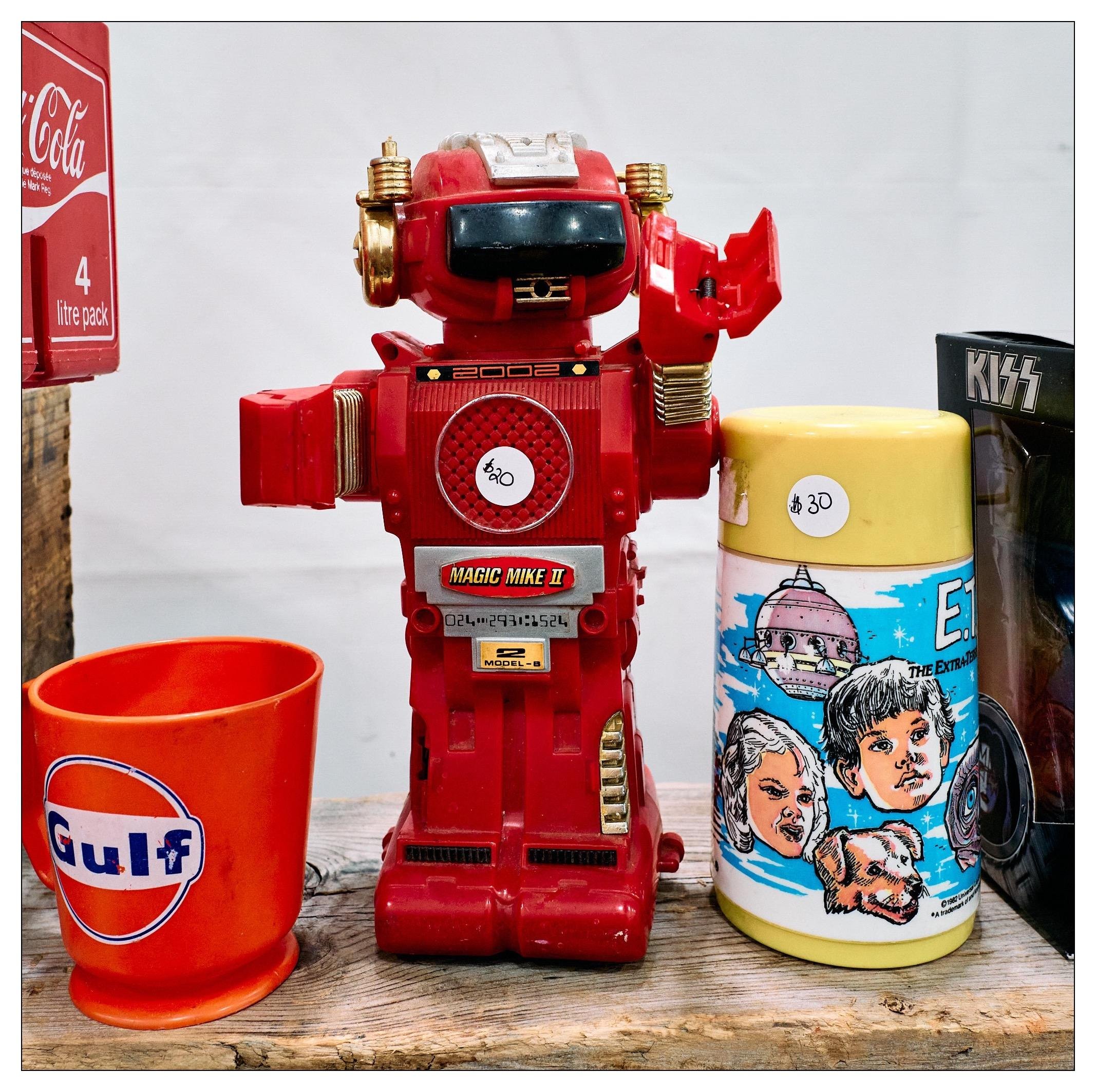 Red Magic Mike 2 robot toy from the early 1980s. On either side are other collectible items such as a Gulf gas station branded cup, an ET thermos, and some other things with CocaCola and Kiss branding.