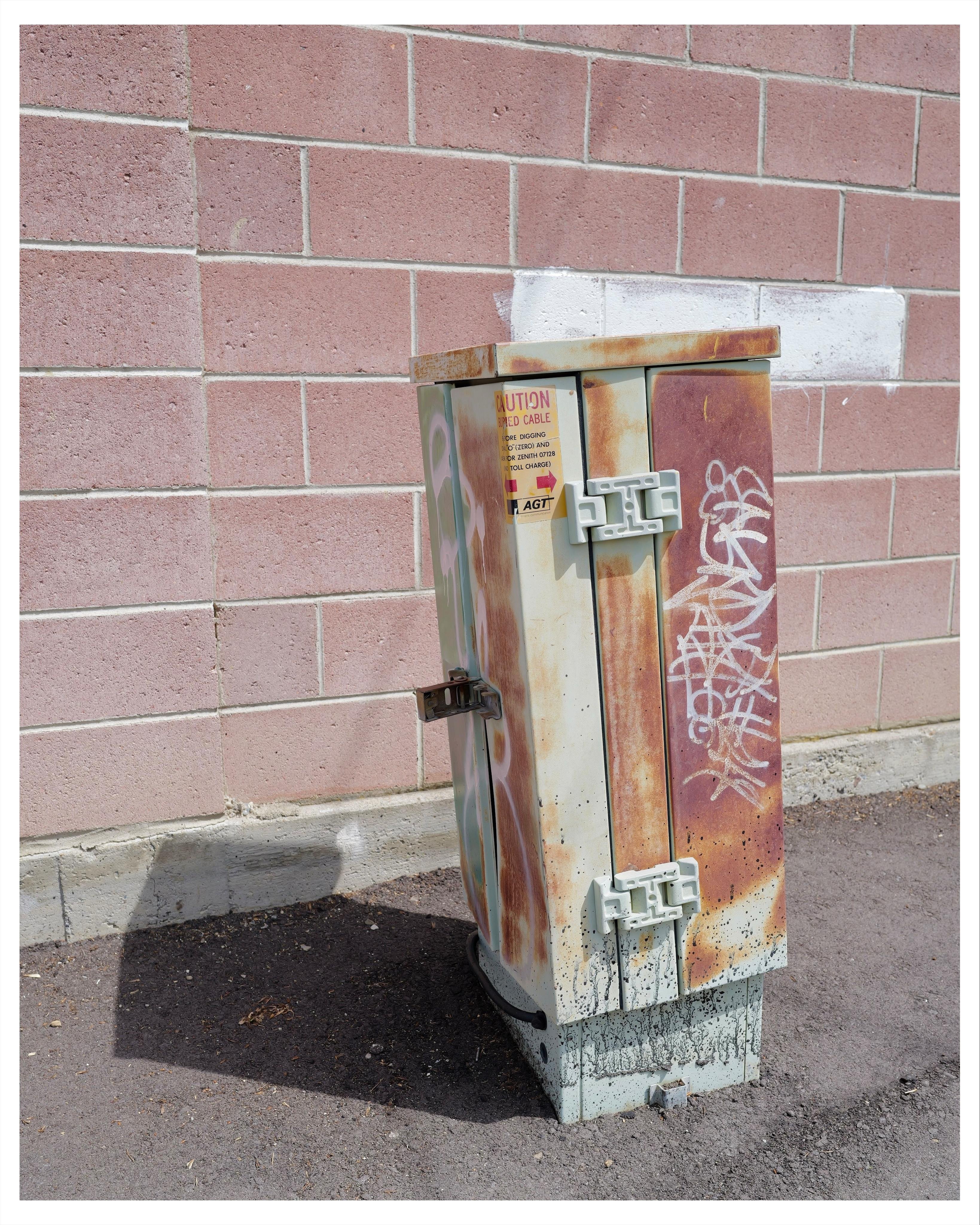 Old, rusty, graffitied telephone junction box in a paved alley.   AGT sticker on it, which hadn’t existed since 1991.

https://en.wikipedia.org/wiki/Alberta_Government_Telephones