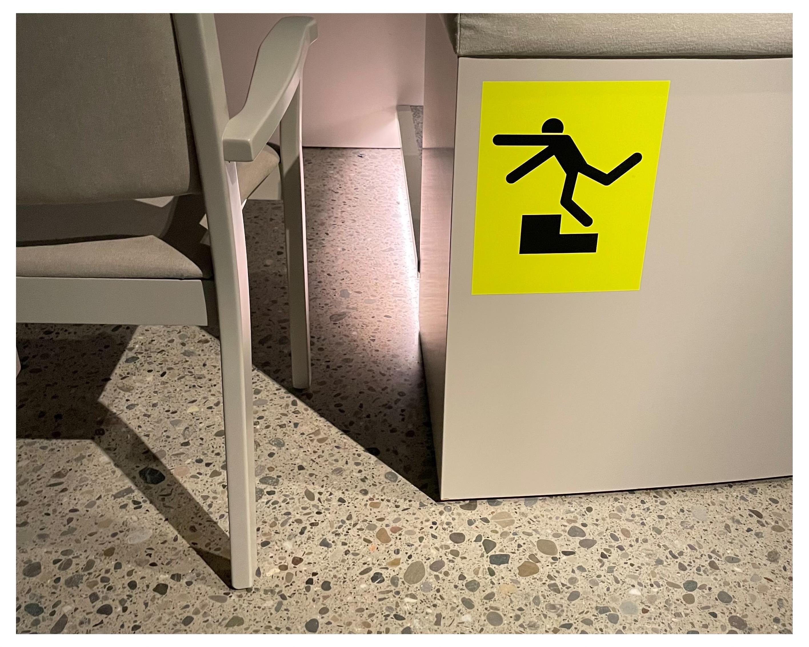 Seating in a museum, featuring a bright yellow and black stick man figure tripping over a step and flying through the air.